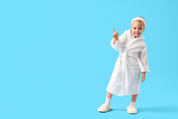 Cute little girl in bathrobe pointing at something on blue background
