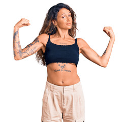 Young hispanic woman with tattoo wearing casual clothes showing arms muscles smiling proud. fitness...