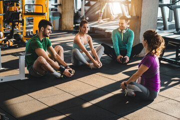 Group of diverse athletic people exercising in a health club. Young friends doing stretching exercises while sitting on the floor in gym. Fitness instructor exercising with a group of three people.