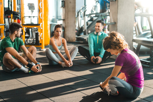 Group of diverse athletic people exercising in a health club. Four cheerful young people having engaging conversation while stretching their legs before training sitting on the floor in gym.