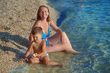 Happy  woman mother and little son  sitting on sea ocean beach at vacation resort  in Porec, Croatia