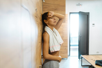 Fototapeta na wymiar Tired athletic woman standing in locker room and taking a break from exercising. Young female feeling menstrual pain after workout.