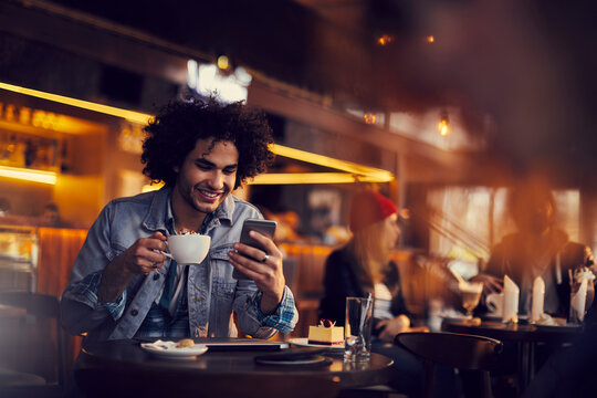 Smiling young man sitting in cafe using smartphone