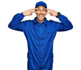 Bald man with beard wearing builder jumpsuit uniform doing peace symbol with fingers over face, smiling cheerful showing victory