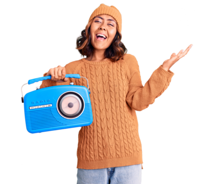 Young beautiful mixed race woman holding vintage radio celebrating victory with happy smile and winner expression with raised hands