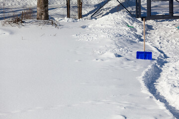 Snow shovel near a cleared path in a snowy area, copy space