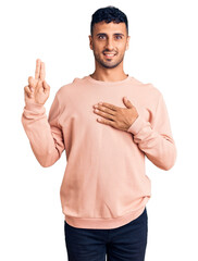 Naklejka premium Young hispanic man wearing casual clothes smiling swearing with hand on chest and fingers up, making a loyalty promise oath