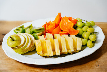 Freshly Sliced Fruit Platter on White Dish. Assorted fresh fruit slices neatly presented on a white...
