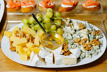Cheese Platter with Honey, Nuts, and Grapes. Elegant cheese selection featuring brie, blue cheese, and cheddar, served with honey, walnuts, and green grapes.