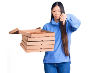 Young beautiful chinese woman holding cardboard boxes of italian pizza with angry face, negative sign showing dislike with thumbs down, rejection concept