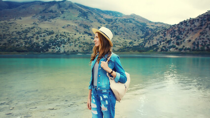 Summer vacation, young woman tourist in straw hat with backpack on lake and mountains background. Greece, island Crete