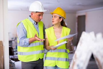 Caucasian man and woman builders discussing project documentation in apartment during repair works.