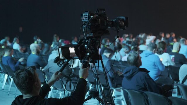Male videographer recording businesspeople attending global workshop in illuminated conference hall