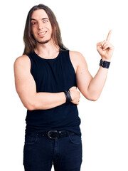 Young adult man with long hair wearing rocker style with black clothes and contact lenses smiling...