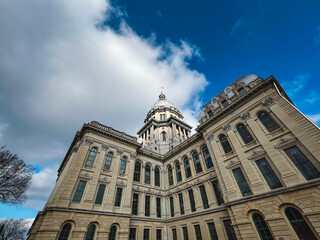 Fototapeta na wymiar Rear views of the Illinois State Capitol Building in Springfield, Illinois, USA. Cloudy blue skies overhead. Sunlight shines down upon the dome of the building.