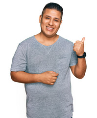 Young latin man wearing casual clothes smiling with happy face looking and pointing to the side...