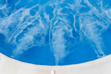Air bubbles from jacuzzi jet in blue water in a pool