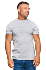 Handsome muscle man wearing casual grey tshirt looking away to side with smile on face, natural expression. laughing confident.