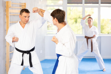 Obraz premium Young guy and man during martial arts karate class train to perform basic blows to opponent with their hands and feet. Preparation of athletes for competitions