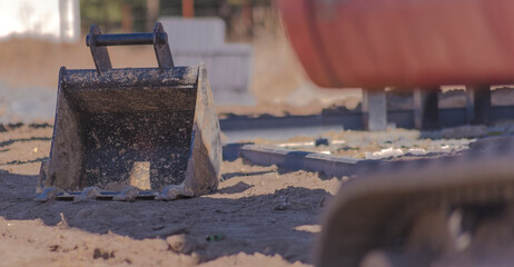 Łyżka małej koparki gąsienicowej leżąca obok maszyny na placu budowy domu. Łyżka z czterema...