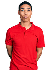 Young hispanic man wearing casual red t shirt making fish face with lips, crazy and comical gesture. funny expression.