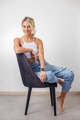 Woman with blonde hair sitting on chair. Lovely millennial lady posing, relaxing indoors. Smile.