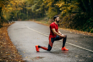 A sportsman is stretching in nature on a roadway on rainy weather.