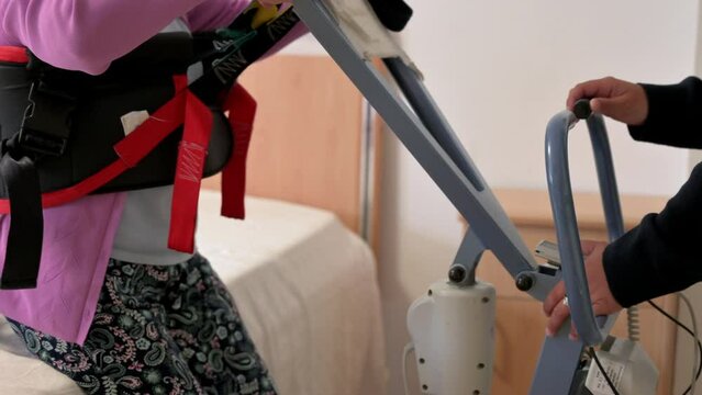 A care staff using a power assist to lifts a patient at nursing home. High quality 4k video.