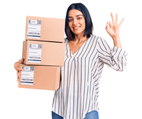 Young beautiful latin woman holding delivery package doing ok sign with fingers, smiling friendly gesturing excellent symbol