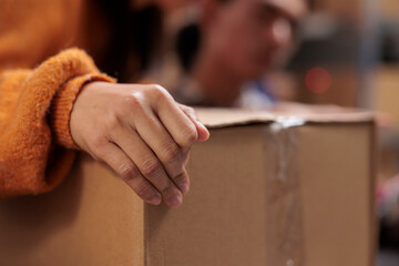 Package handler arm holding packed cardboard box in industrial warehouse. Storehouse employee...