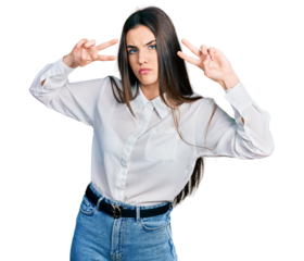 Young brunette teenager doing peace gesture close to eyes relaxed with serious expression on face. simple and natural looking at the camera.