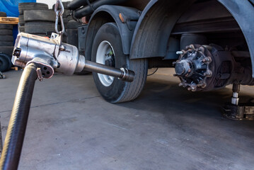 Compressed air tool to remove wheel bolts in a tire shop, with a truck with a wheel removed.