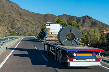 Truck with a hole in its trailer to transport a steel coil, held with several slings, rear view.