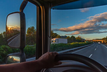 View from the driver's seat of a truck of a highway at dawn and the sun reflected in the rearview mirror.