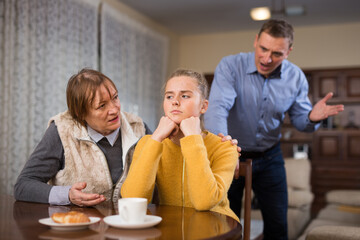 Frowning teenage girl listening to reprimanding from her father and grandmother at home