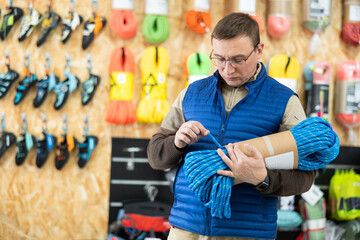 Fototapeta na wymiar Male tourist chooses and buys climbing rope for an winter hike in a tourist equipment store