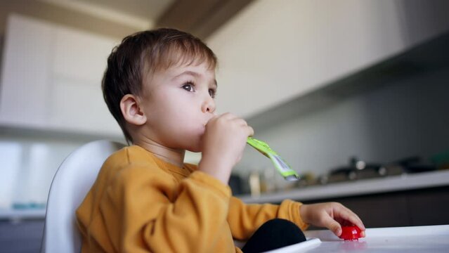 Adorable cute toddler boy eating puree fruit. Child holds the doy pack in his mouth. Low angle view. Close up.