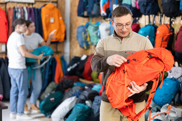 Buyer man chooses autumn backpack in store for long hikes and climbing mountains. Travel accessories of different price categories.