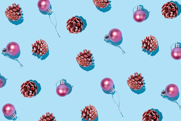 Creative holiday pattern made of pine cones and pink ornament balls on bright blue...