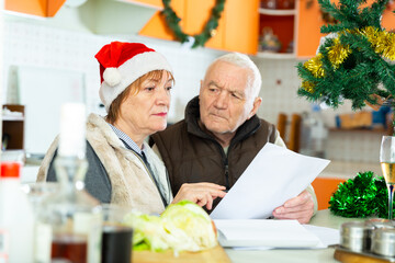 Chagrined mature couple working with papers at home before Christmas