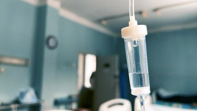 Drip chamber in an IV hanging on a stand against the background of blurred medical beds in a clinic ward