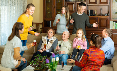 Happy large family gathered in parental home for family party, cheerfully talking in cozy living...