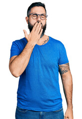 Hispanic man with beard wearing casual t shirt and glasses bored yawning tired covering mouth with hand. restless and sleepiness.