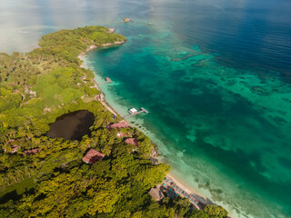 Aerial drone view from above of the tropical Caribbean island with lush green palm trees forests and sandy beaches surrounded with crystal clear turquoise shallow ocean water.