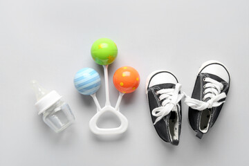 Baby bottle, shoes and rattle on grey background
