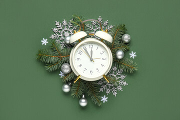 Alarm clock with Christmas balls and fir branches on green background