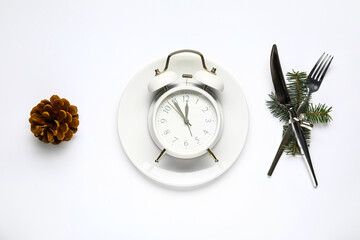 Plate, cutlery with alarm clock and Christmas tree branches on white background
