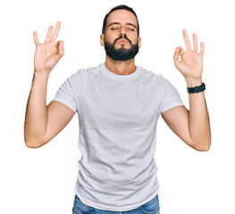 Naklejka premium Young man with beard wearing casual white t shirt relaxed and smiling with eyes closed doing meditation gesture with fingers. yoga concept.