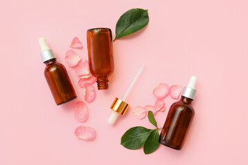 Bottles of cosmetic oil with rose extract, petals and leaves on pink background