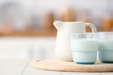 Wooden board with ceramic jug and glasses of milk on white tile table